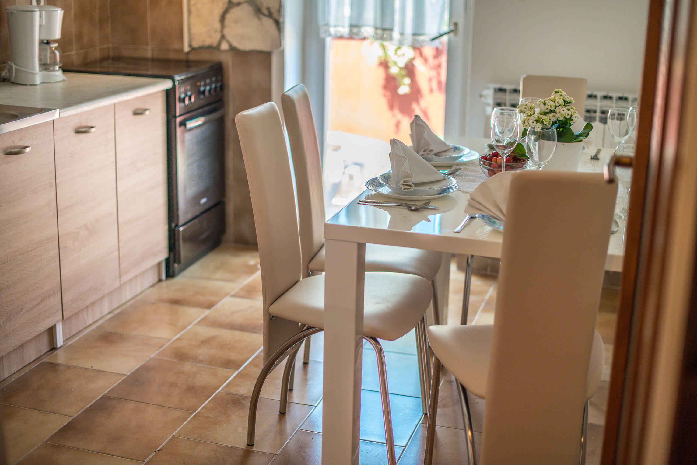 A modern kitchen with white cabinets, a built-in oven, and a dining area with a glass table and white chairs.