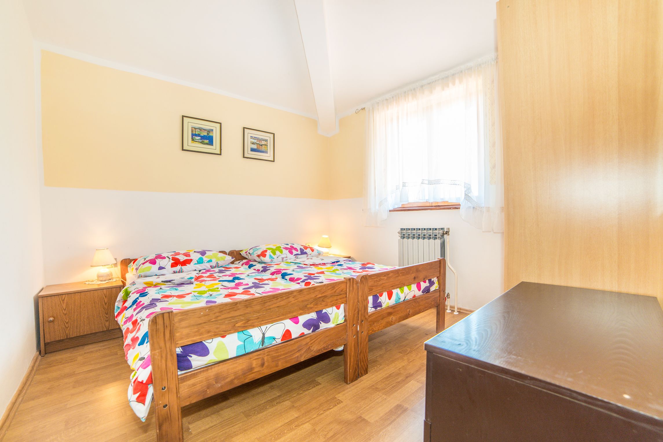 A bedroom with a wooden bed, a nightstand, a radiator, and two framed pictures on the wall.