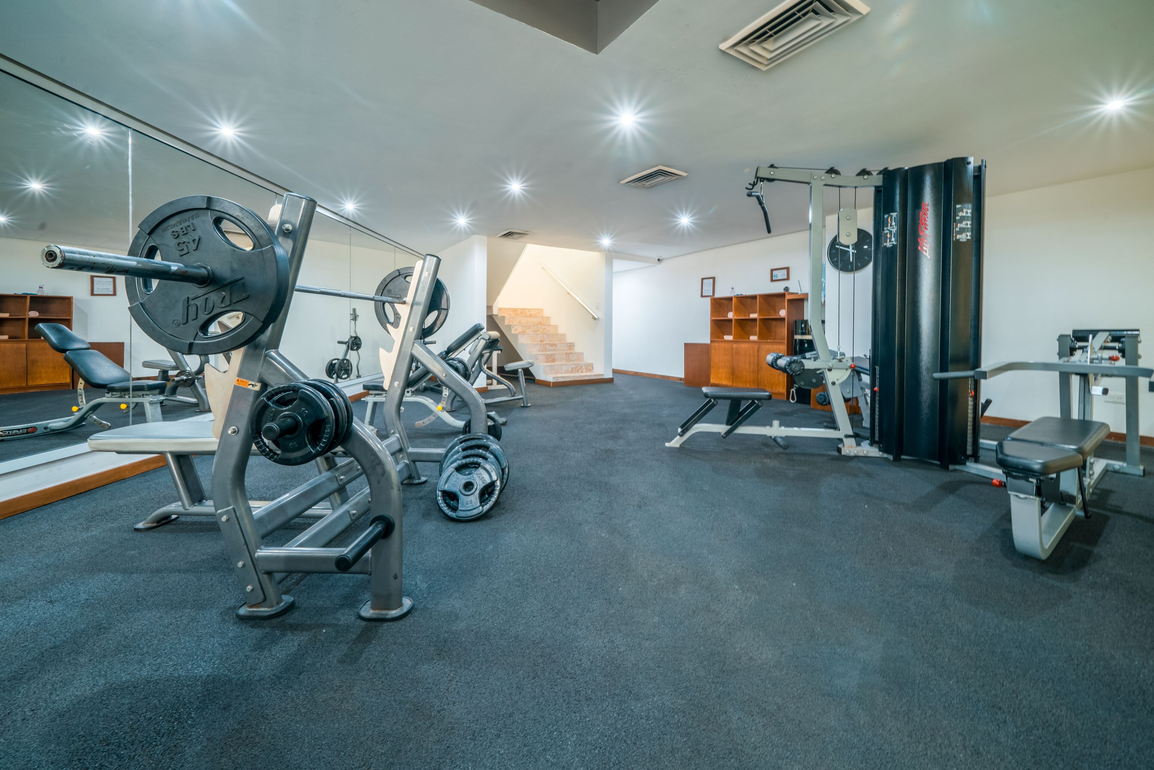 A gym with weightlifting equipment, a staircase, and a mirror.