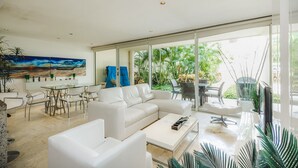 A modern living room with a white sectional sofa, a glass dining table, and a large window offering a view of greenery. - Elements GH8 by NAS (Playa del Carmen)