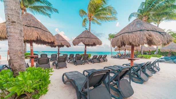 A beachside lounge with thatched umbrellas, lounge chairs, and a view of the ocean. - Elements GH8 by NAS (Playa del Carmen)