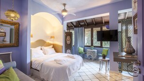 A well-lit bedroom with a bed, a TV, a small table with a plant, and a decorative vase. - Alterra Vita (Sithonia)