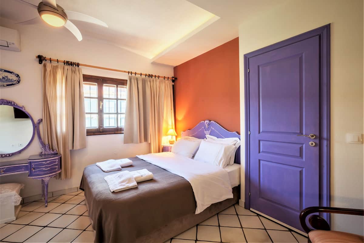 A hotel room with a bed, a window with curtains, a bedside table, a mirror, and a door.