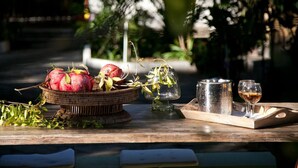 A wooden table with a wicker basket containing fruits, a metal pitcher, and a glass of wine. - Alterra Vita (Sithonia)