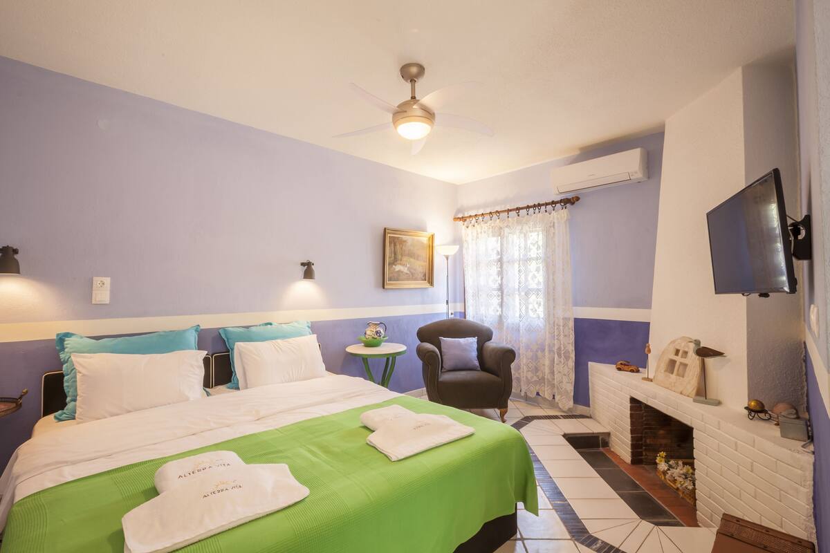 A hotel room with a bed, a chair, a small table, a fireplace, and a television.