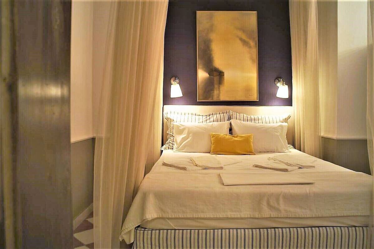 A neatly made bed with white linens and a single yellow pillow, flanked by two bedside lamps.