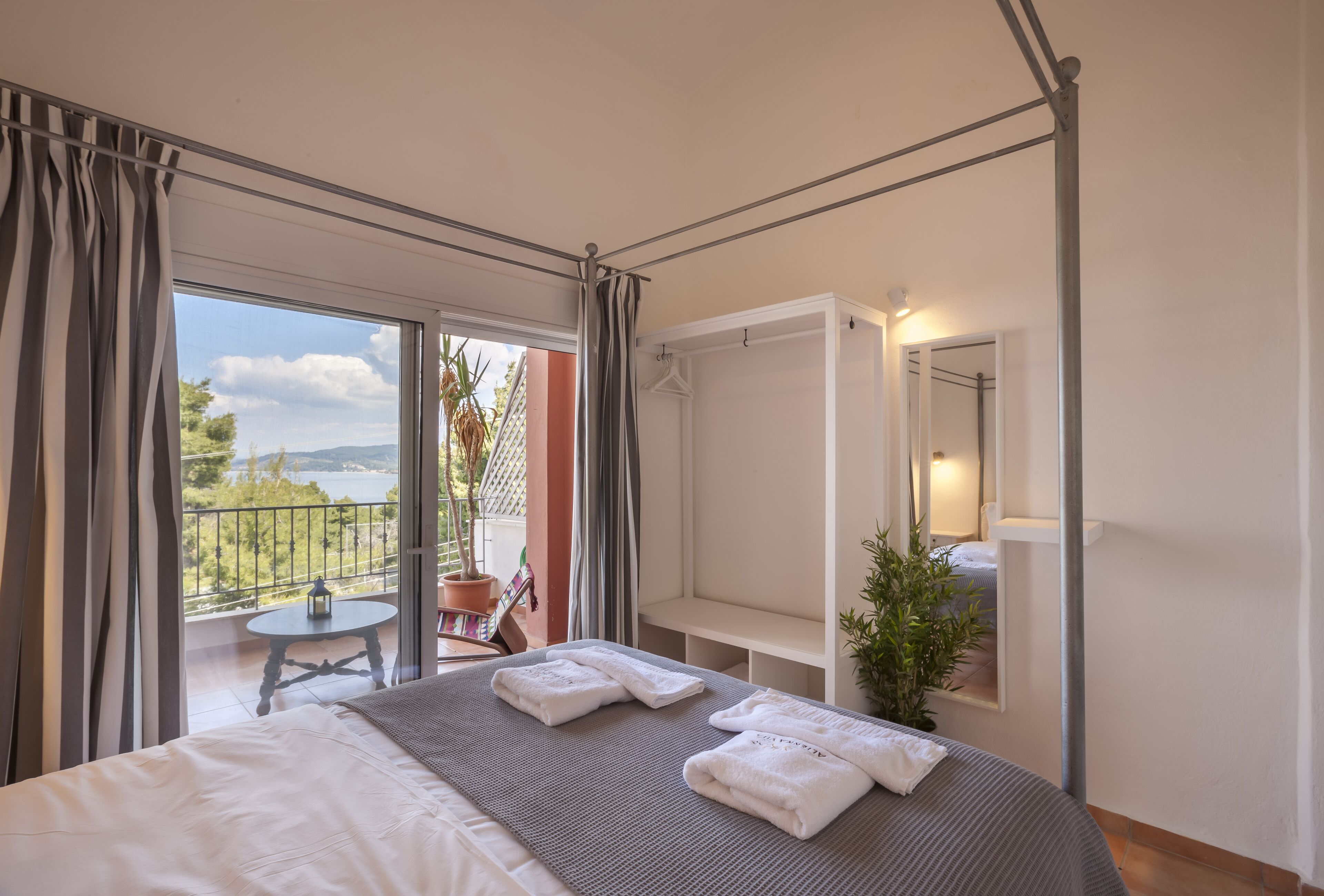 A bedroom with a bed, a balcony with a table and chairs, and a hanging coat rack.