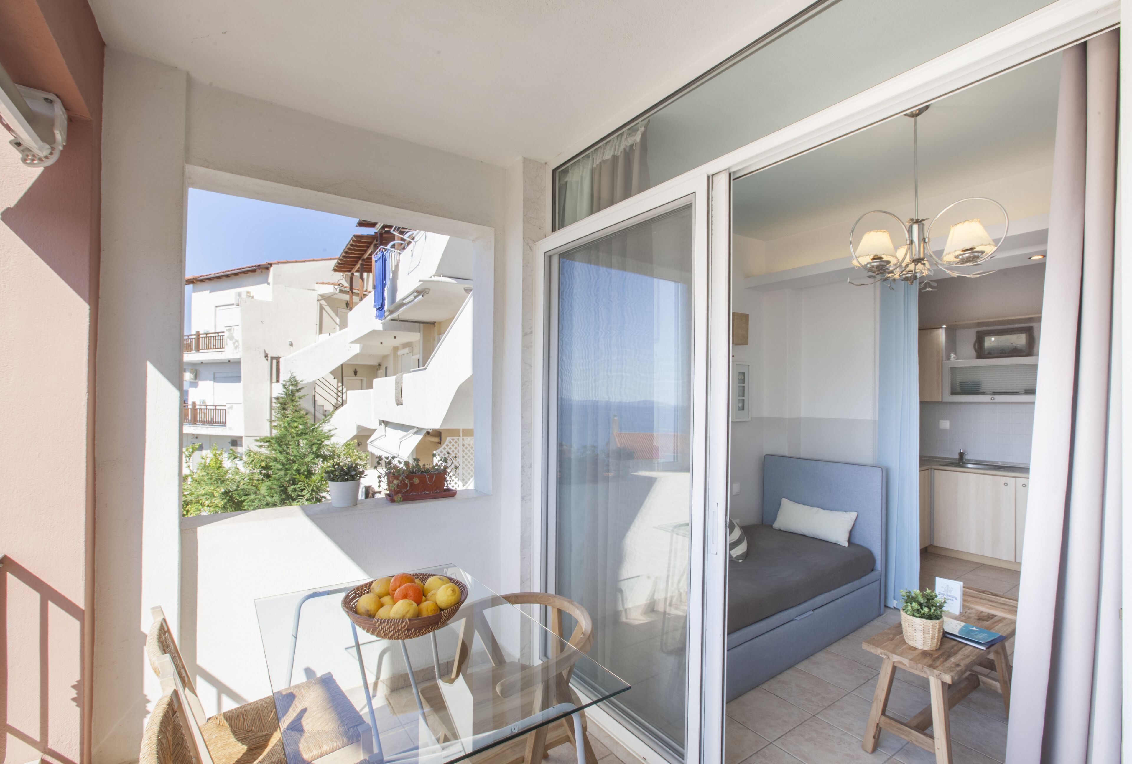 A balcony with a glass table, a wicker basket with fruits, and a view of a residential building.