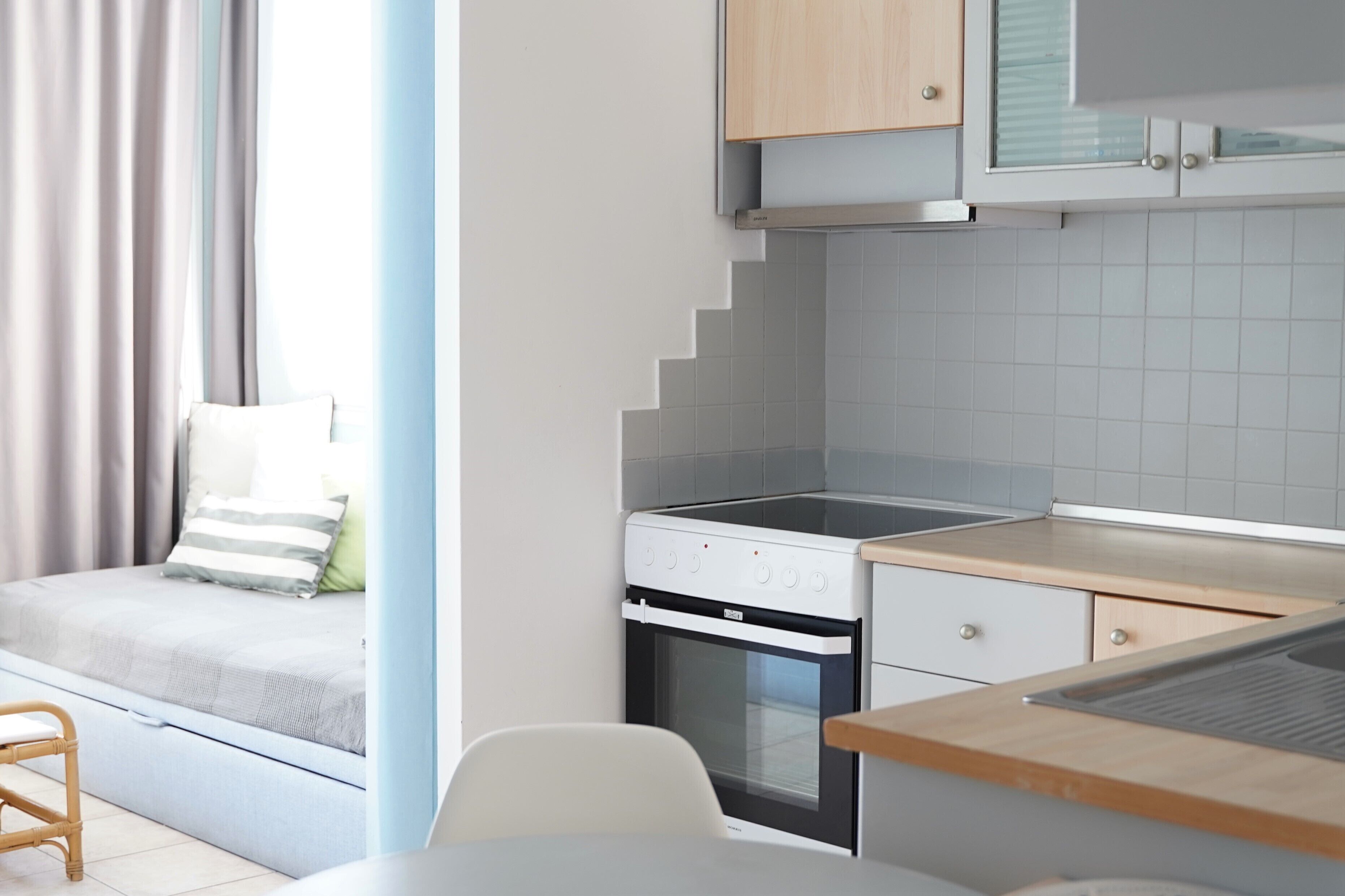 A compact kitchen with a built-in oven, a dining area with a table and chairs, and a bed with a view of the outside.