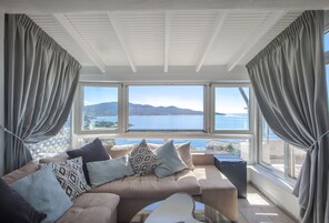 Una sala de estar moderna con un sofá color beige, cojines estampados y vistas al mar a través de amplios ventanales.