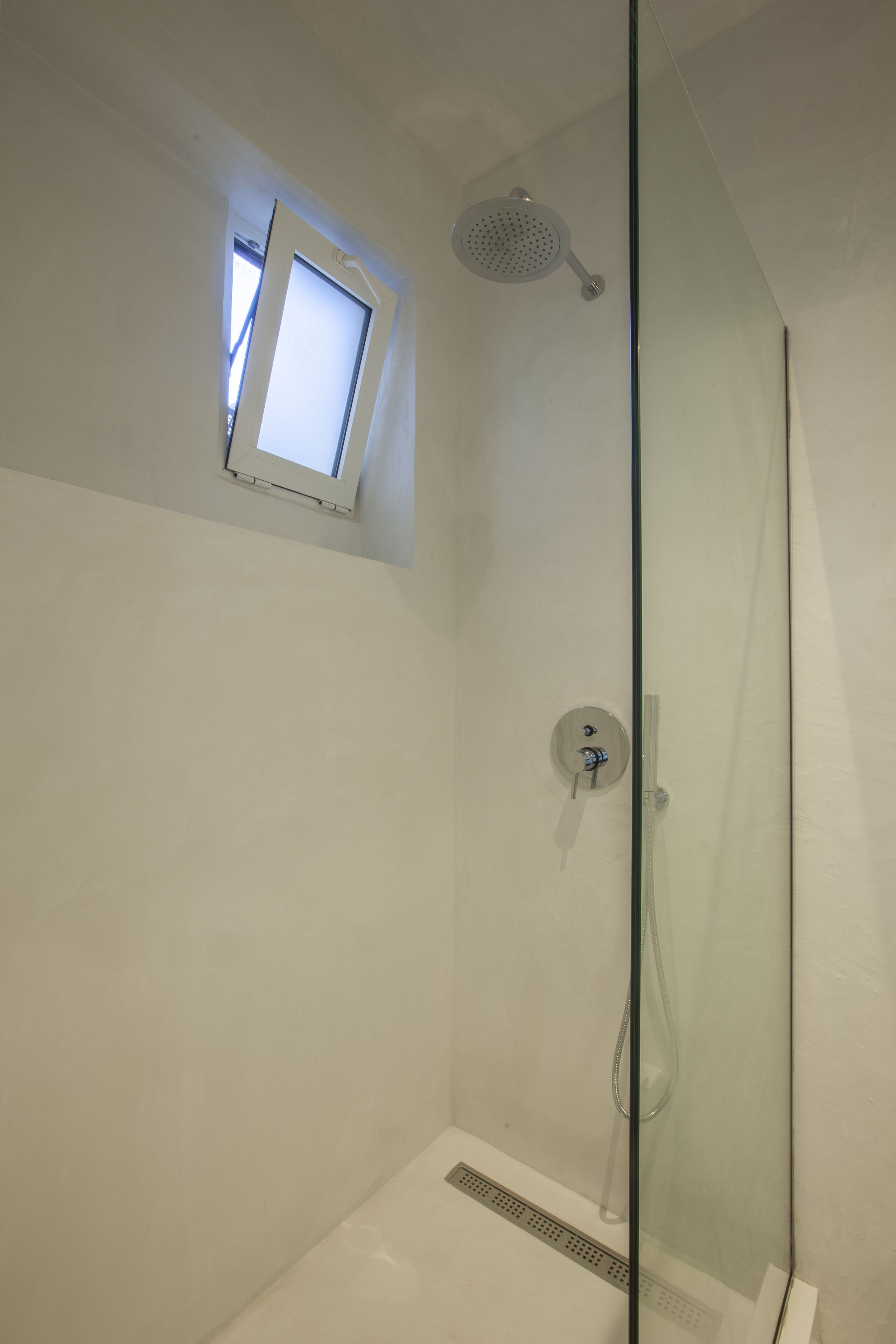A glass-enclosed shower with a handheld showerhead and a small window above it.