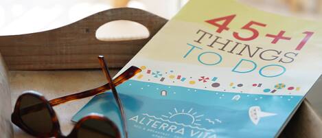 A book titled "45+1 Things to Do" with a beach and sun illustration, placed on a wooden surface with a pair of sunglasses beside it.