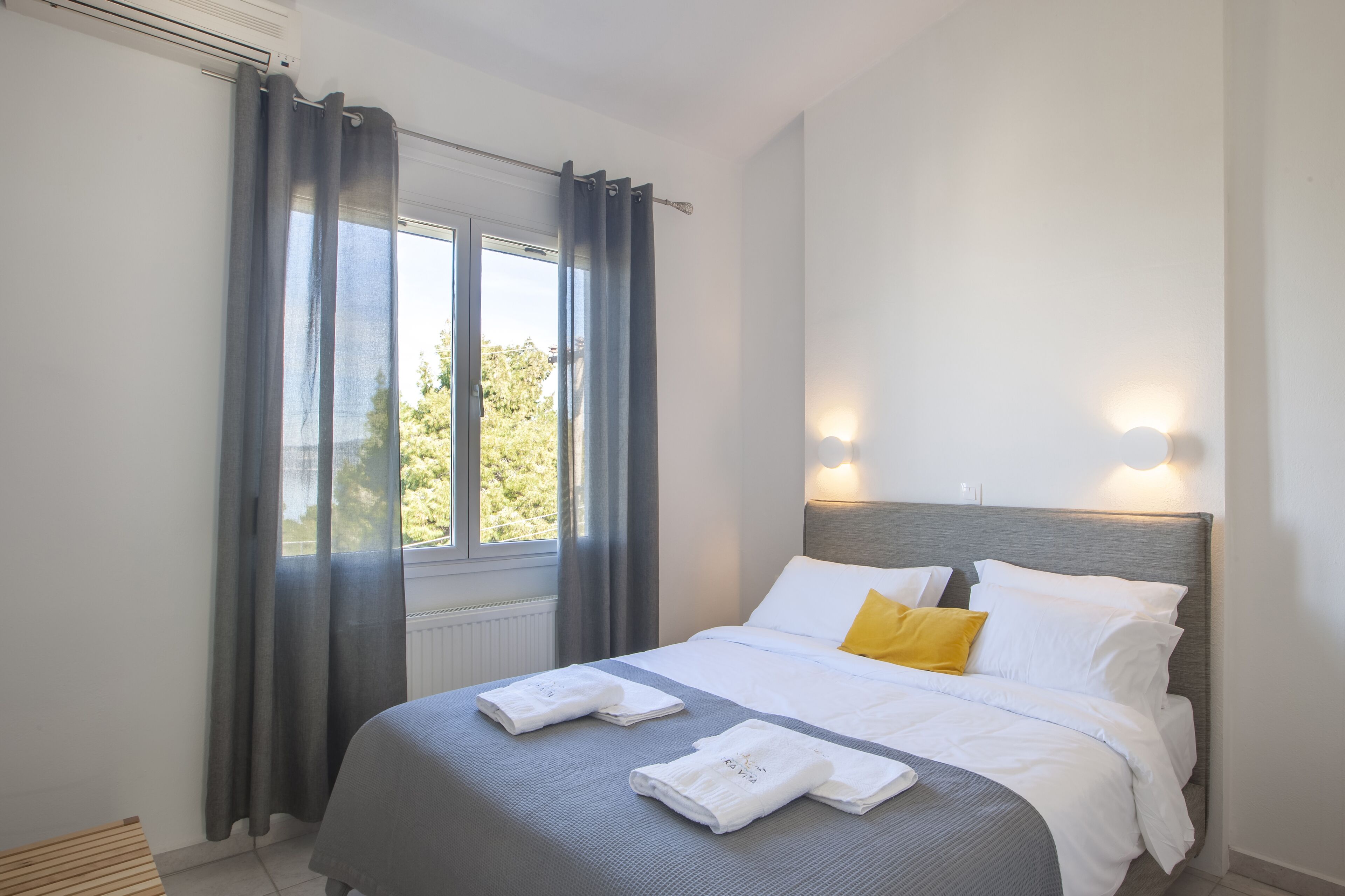 A neatly made bed with white and gray bedding, a single yellow pillow, and two folded towels.
