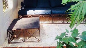 Une véranda avec un canapé bleu foncé, une petite table et un élément décoratif mural représentant un soleil.