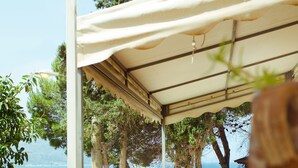 A covered outdoor area with a view of the sea, surrounded by trees and greenery.