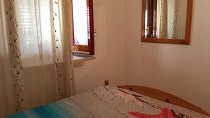 A bedroom with a bed, a window, and a mirror on the wall.
