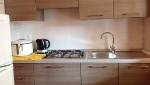 A kitchen with wooden cabinets, a gas stove, a kettle, and a sink.