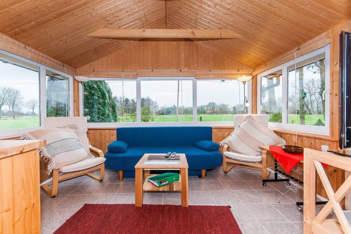 A cozy room with a blue sofa, two chairs, a small table, and large windows offering a view of the outdoors.