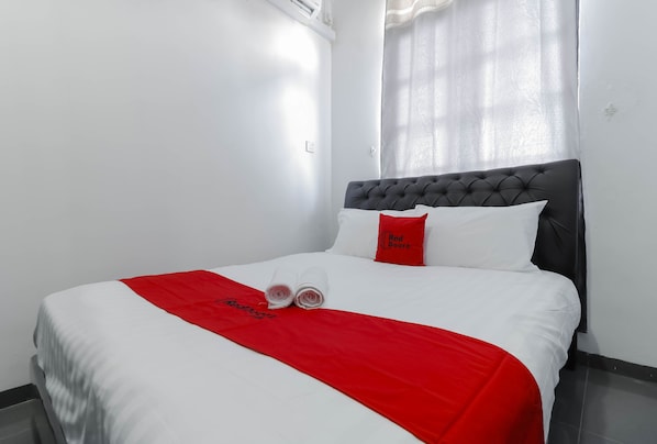 A neatly made bed with white and red bedding, a red pillow, and a rolled towel.