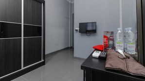 A hotel room with a sliding door, a television mounted on the wall, a desk with a telephone, a red pillow, and bottled water. - RedDoorz Plus near Batam City Square (Batam)
