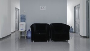A hallway with two black armchairs, a water dispenser, and a no-smoking sign on the wall. - RedDoorz Plus near Batam City Square (Batam)