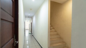 A hallway with a wooden door, tiled floor, and a staircase with beige steps. - RedDoorz @ Nagoya Indah (Batam)