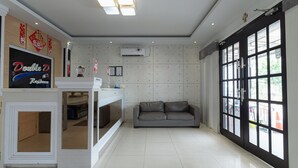A modern hotel lobby with a reception desk, a grey sofa, and large windows. - RedDoorz @ Nagoya Indah (Batam)