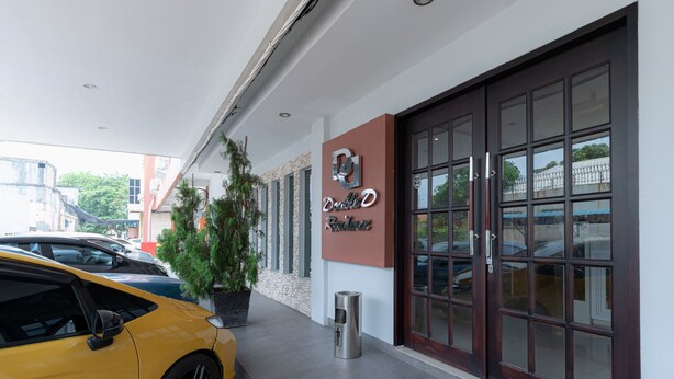 A hotel entrance with a modern facade, a yellow car parked outside, and a potted plant near the entrance. - RedDoorz @ Nagoya Indah (Batam)