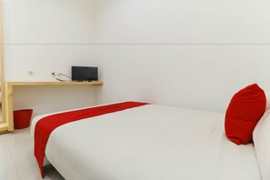 A neatly made bed with a white and red bedspread, a red pillow, and a small wooden shelf with a black object on it. - RedDoorz Plus @ Kapuk Business Park (Jakarta)