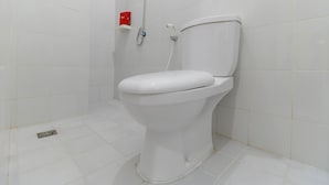 Inodoro blanco con cabezal de ducha y dispensador de jabón rojo en un baño con azulejos blancos.