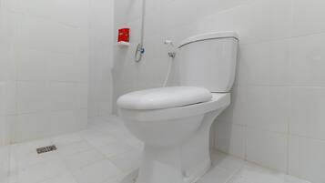 A white toilet with a showerhead and a red soap dispenser in a bathroom with white tiles.