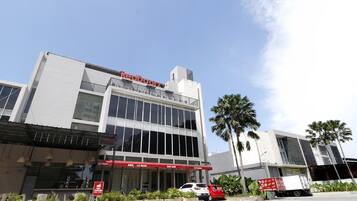A modern building with a large glass facade, a red awning with the text "BBQ LA MIAMI," and a sign indicating "OPEN."