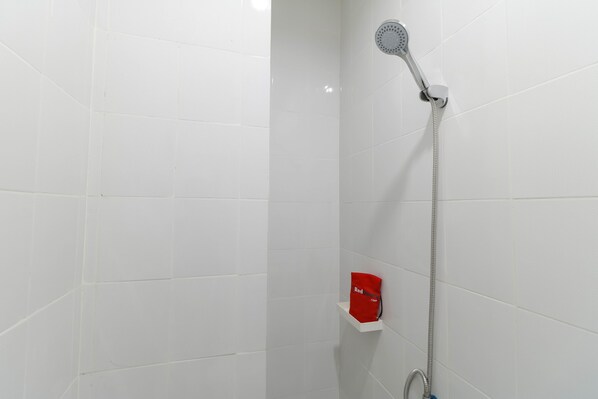 Une salle de bain avec des murs recouverts de carreaux blancs, une douche avec un pommeau de douche amovible et un distributeur de savon rouge posé sur une étagère blanche.
