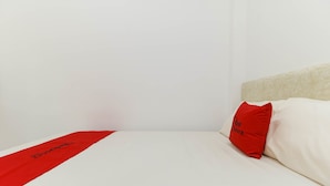 Una cama bien hecha, con un colchón blanco y un corredor rojo.