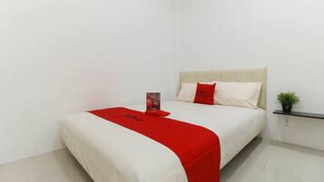 A neatly made bed with a red accent, a small bedside table with a plant, and a wall-mounted shelf.