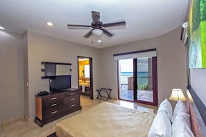 Un dormitorio con cama, televisor en una cómoda, ventilador de techo y balcón con vistas.