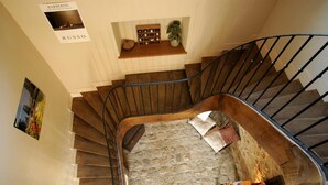 A spiral staircase with a stone floor, a wooden shelf with books and a plant, and a sign reading "RUSSO". - Ferme D'Orsonville (Villiers-en-Bière)