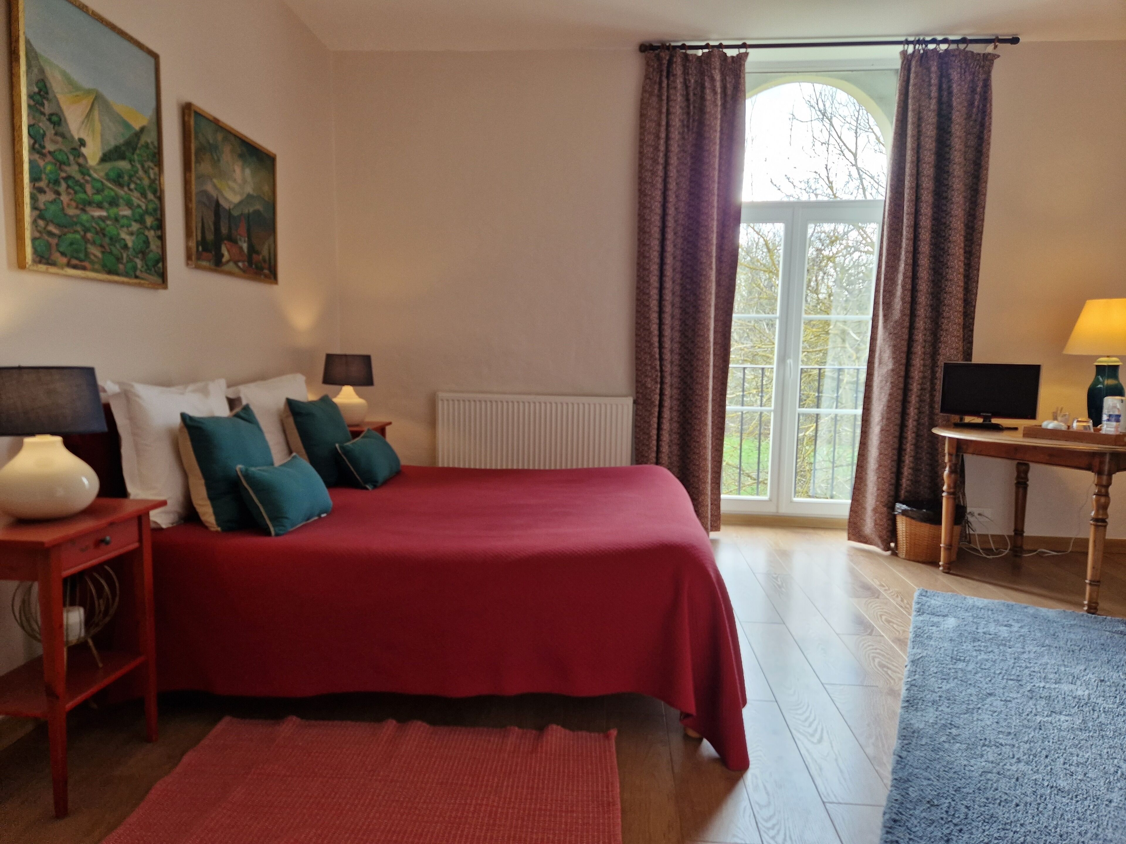 Une chambre à coucher avec un grand lit, deux tables de chevet, un bureau avec un ordinateur et une fenêtre avec des rideaux.