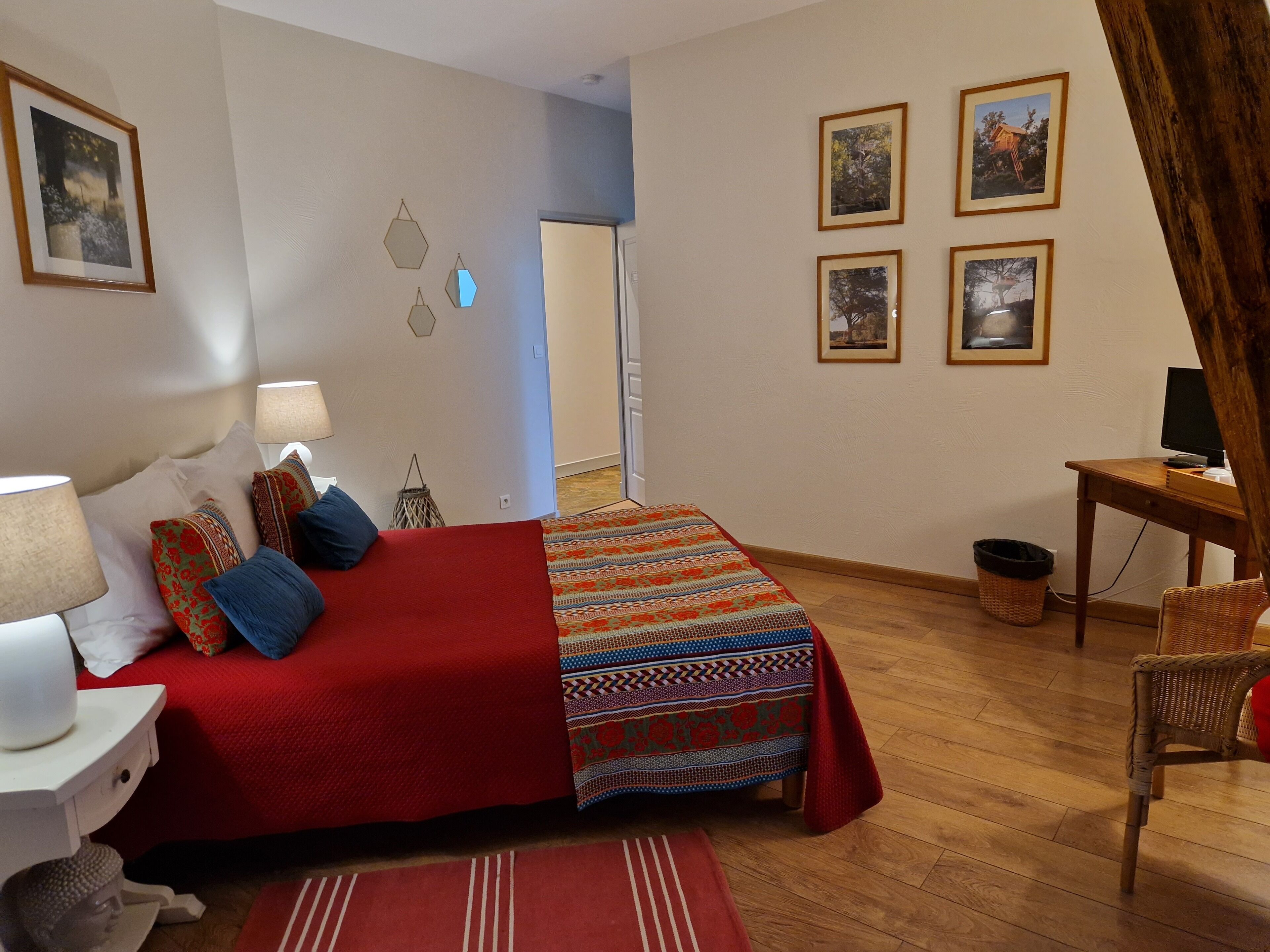 A bedroom with a bed, bedside lamps, a desk, a chair, and framed pictures on the wall.