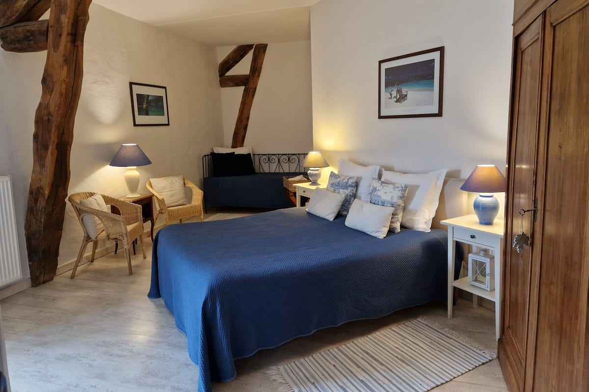 Un dormitorio con una cama grande, dos mesitas de noche con lámparas, una silla y estructura de vigas de madera.