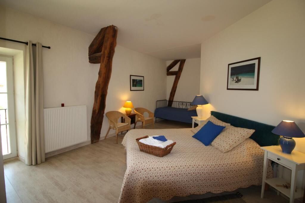 Une chambre à coucher avec un lit, des lampes de chevet, une chaise, une table et une fenêtre avec des rideaux.