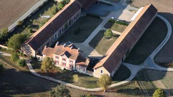 An aerial view of a large, rectangular building with a central courtyard, surrounded by open fields and a few trees.