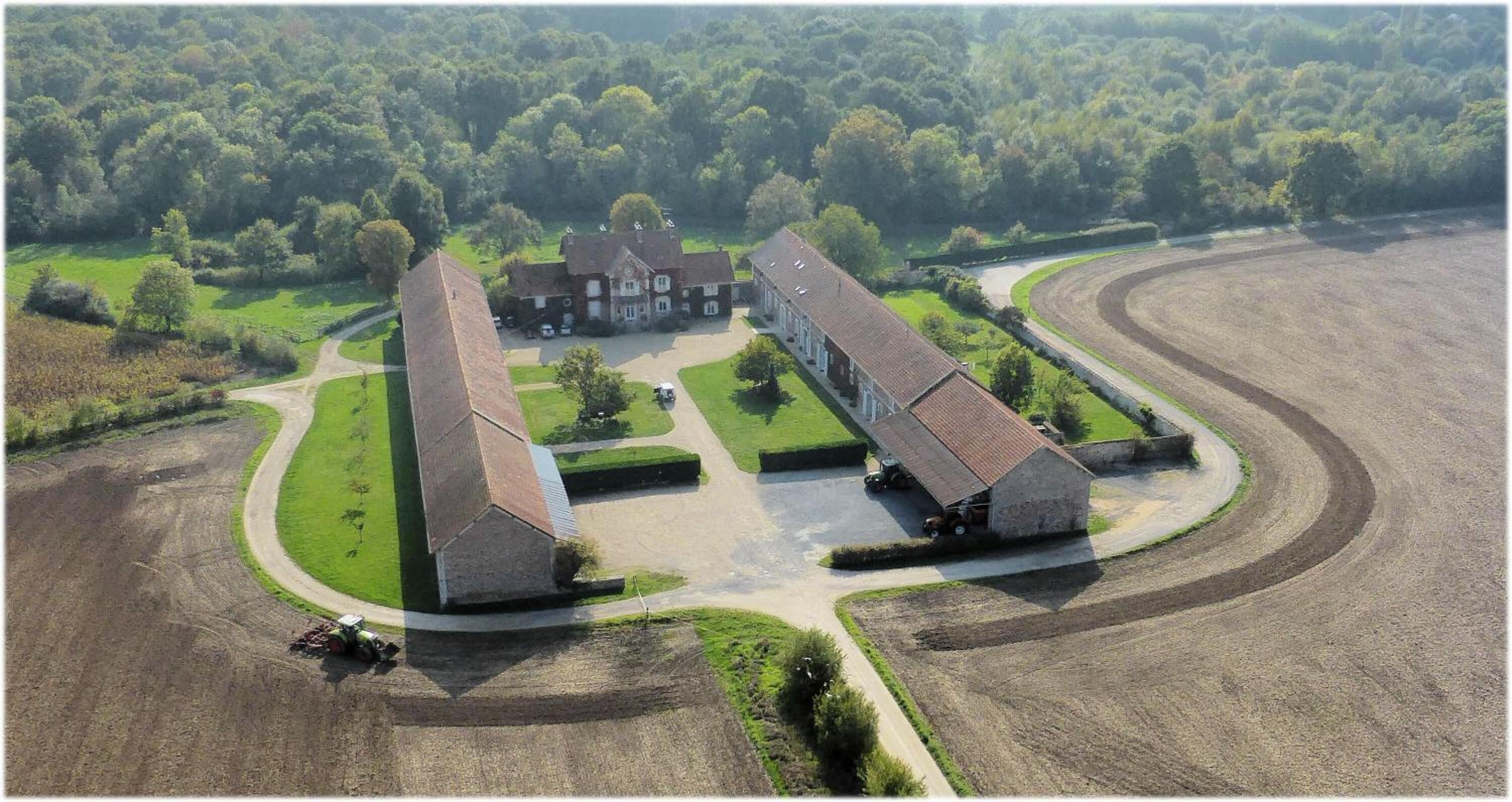 An aerial view of a large estate with multiple buildings, a winding driveway, and surrounding fields.