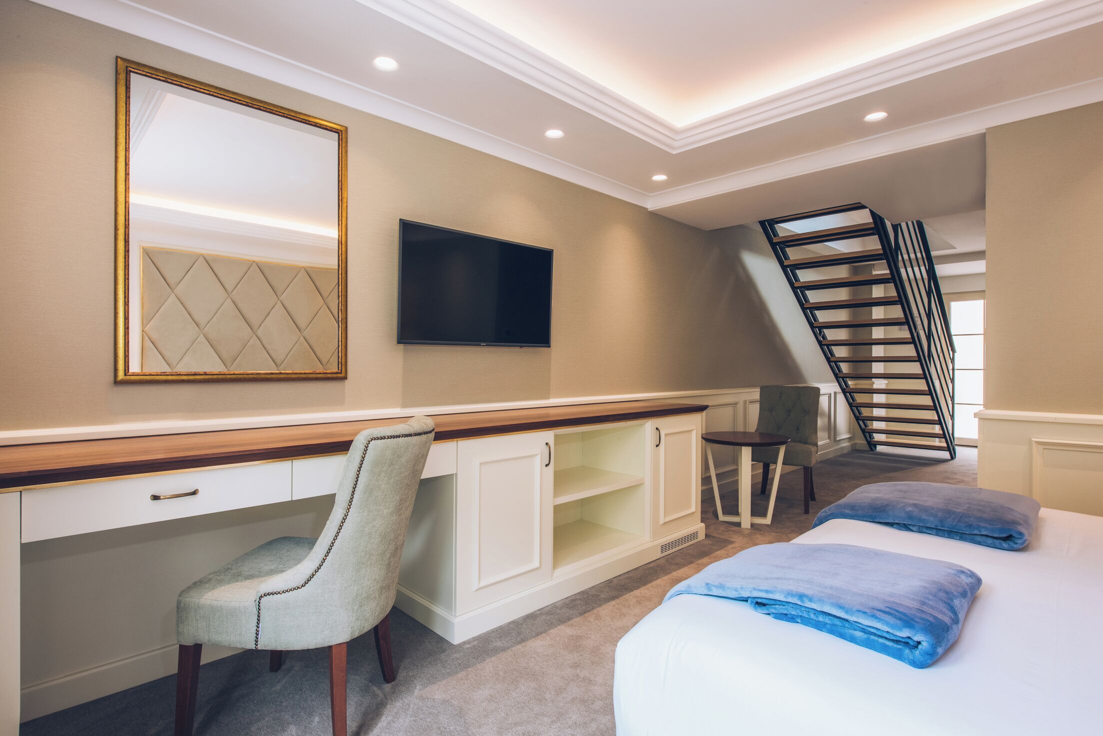 A hotel room with a desk, chair, bed, and a TV mounted on the wall.