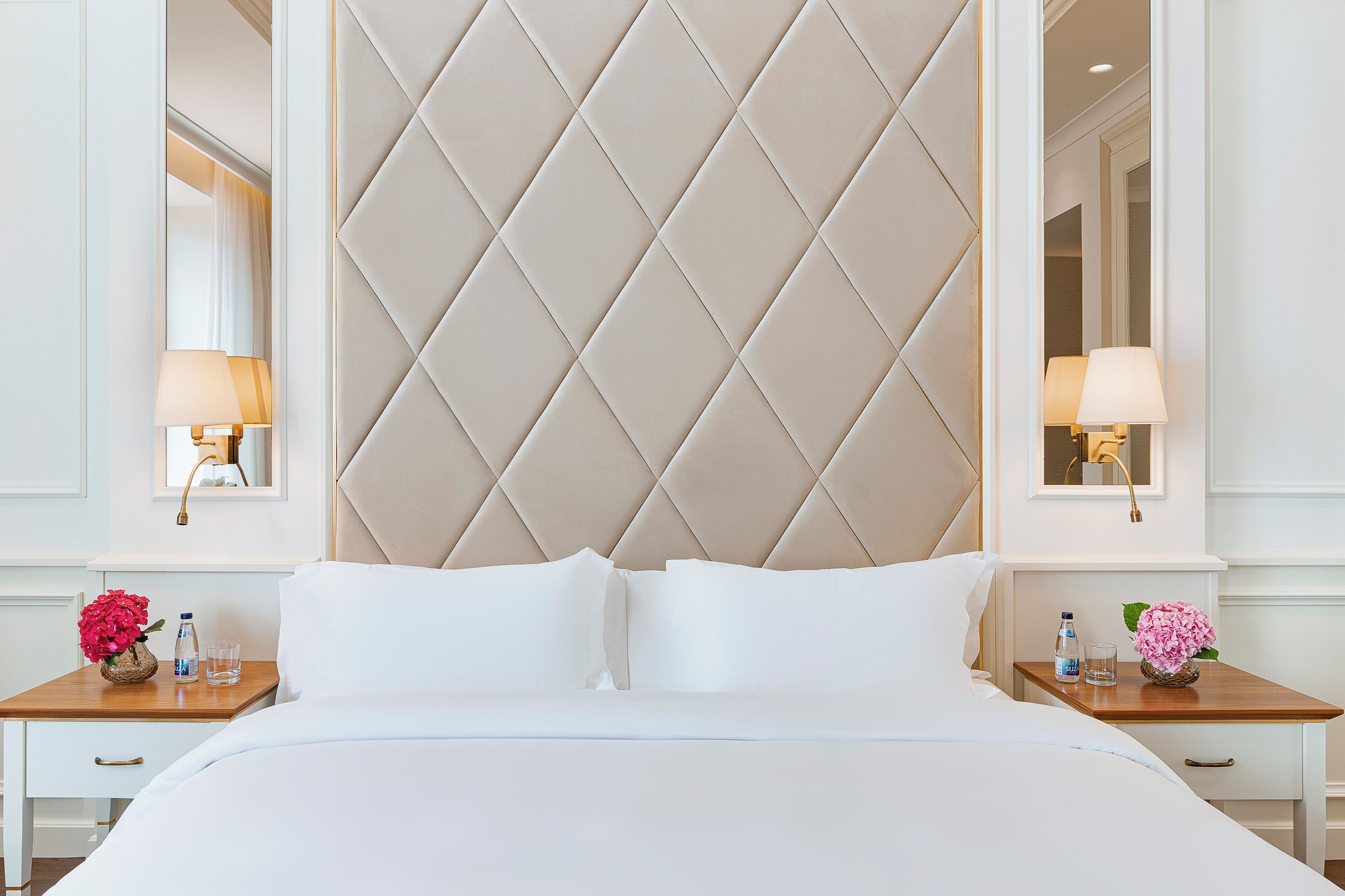 A hotel room with a large bed, a headboard with a diamond pattern, bedside tables with lamps, and a mirror.