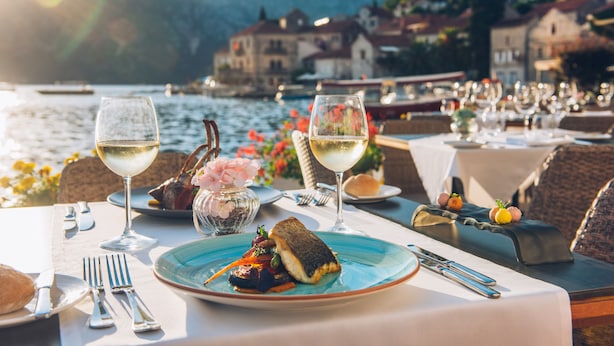 A table set for a meal with a view of a lake and buildings in the background. - Heritage Grand Perast (Perast)