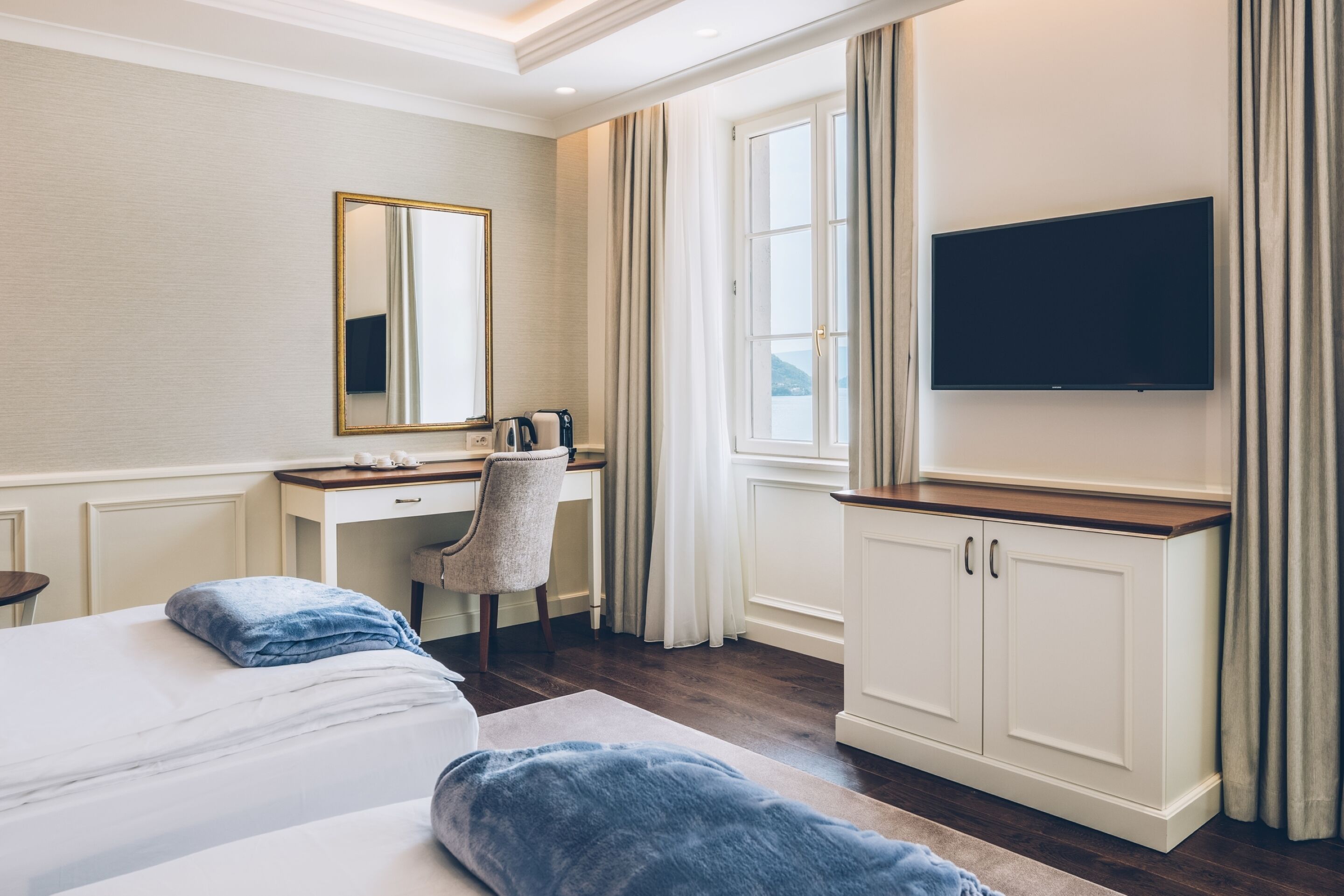 A hotel room with a bed, a desk, a chair, a television, and a window with curtains.