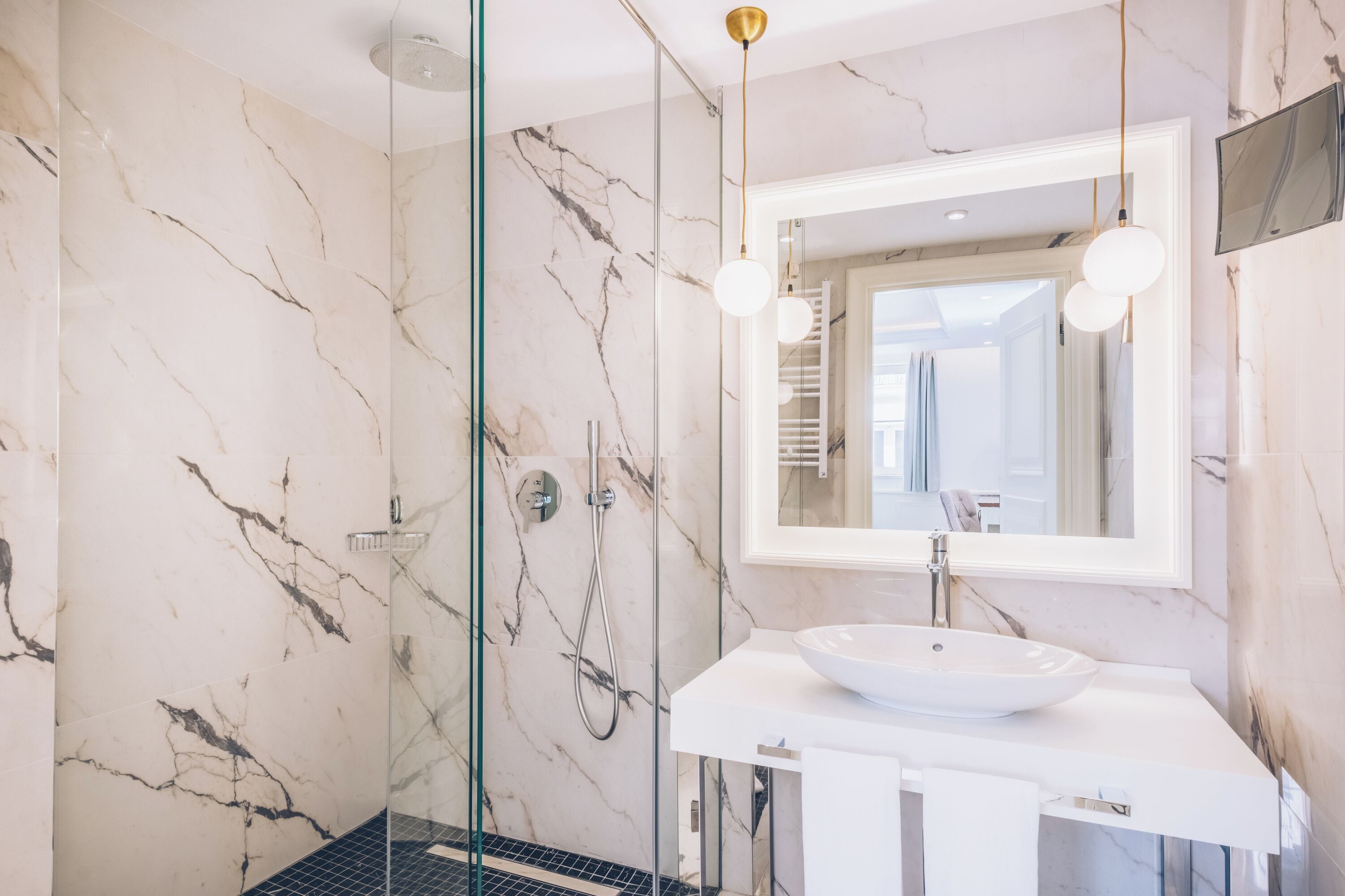 Un baño moderno con cabina de ducha de vidrio, un lavabo blanco y un espejo grande.