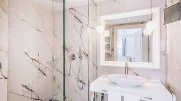 Un baño moderno con cabina de ducha de vidrio, un lavabo blanco y un espejo grande.