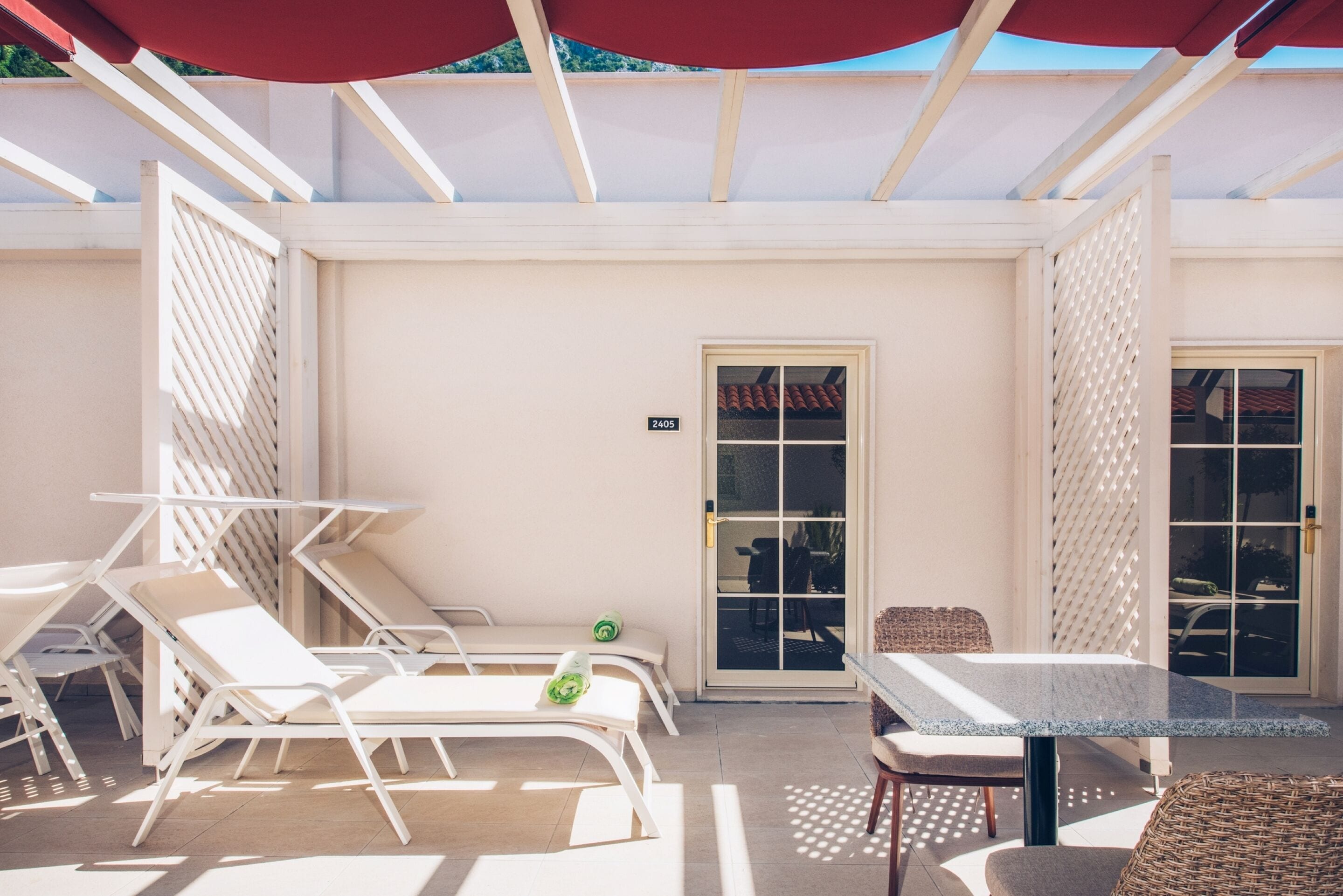 Un espacio de estar al aire libre cubierto con sillones reclinables y una mesa, una puerta con un número, y vista a la calle.